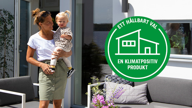 Mamma håller i sitt barn framför sitt hus byggt med klimatpositiva byggprodukter