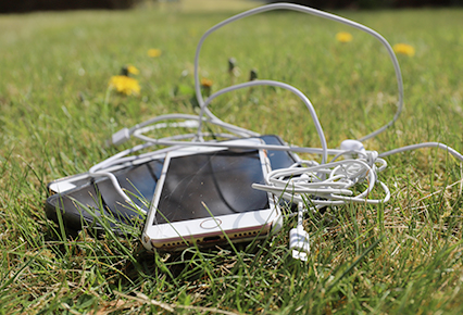 Mobiltelefon med sladd som ligger i gräset